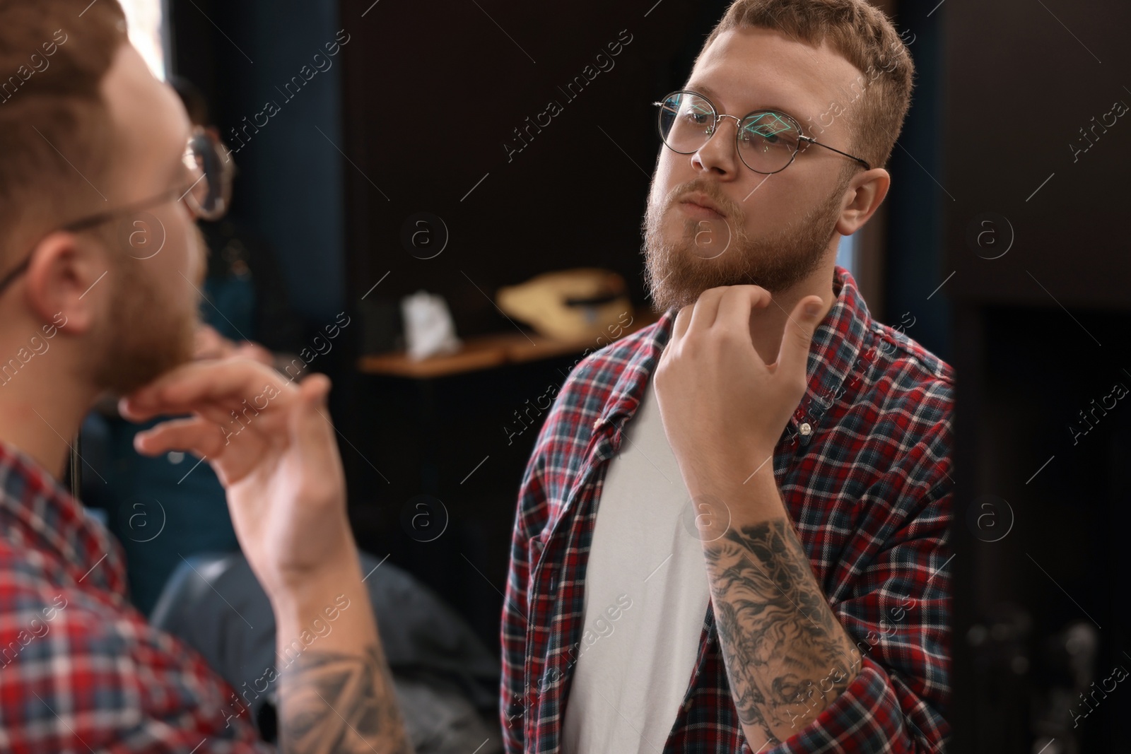 Photo of Young bearded man near mirror in barbershop