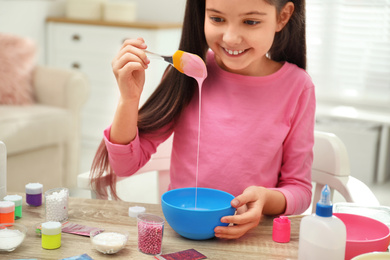 Photo of Cute little girl mixing ingredients with silicone spatula at table. DIY slime toy