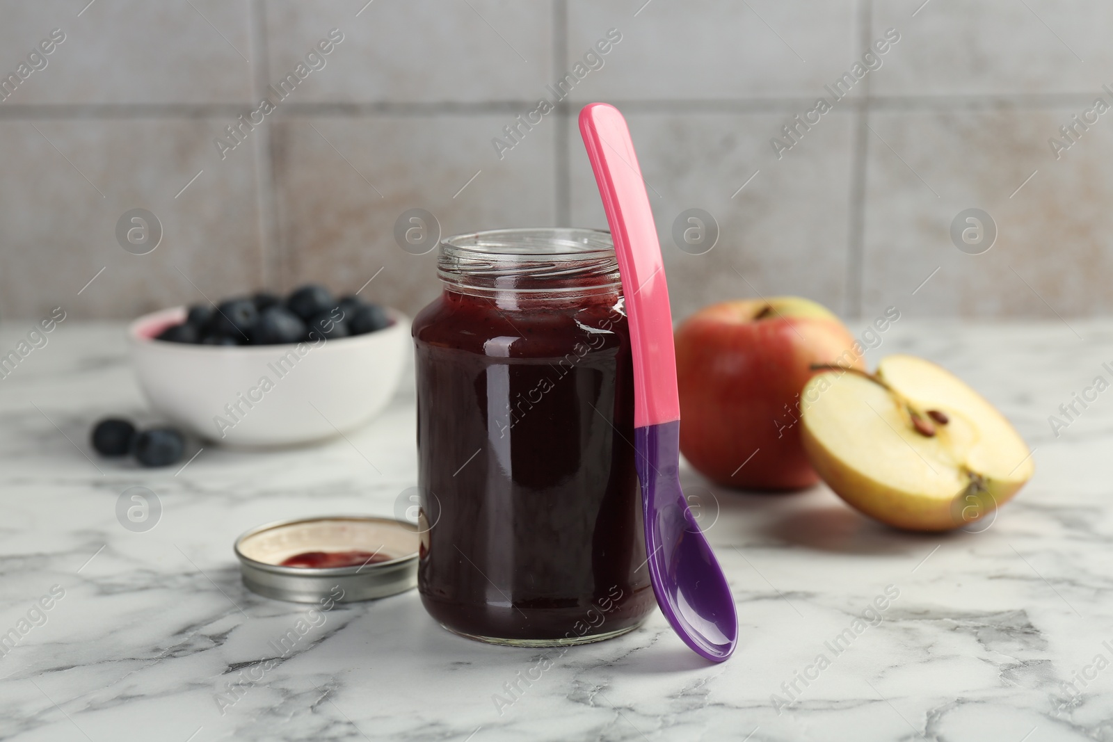 Photo of Tasty baby food in jar and spoon on white marble table