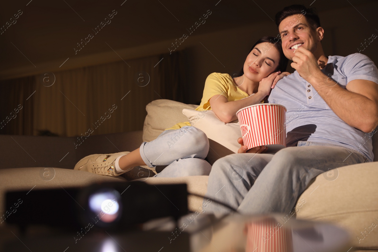 Photo of Couple watching movie with popcorn on sofa at night, space for text