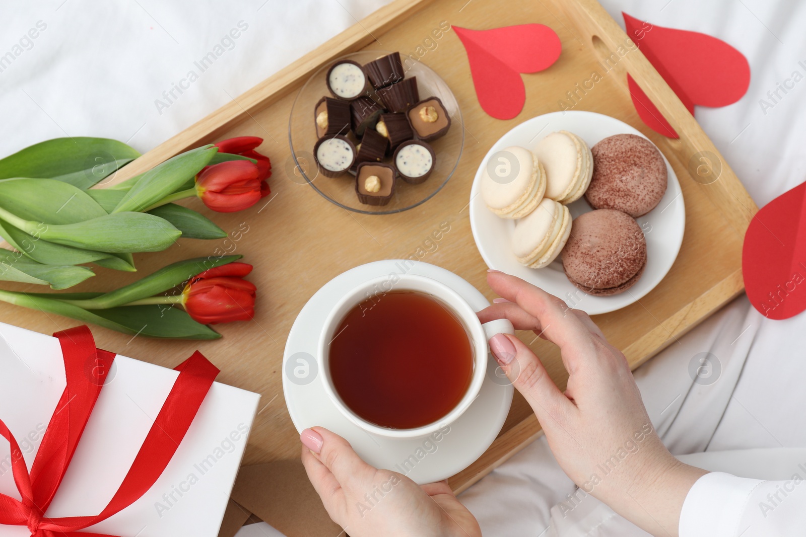 Photo of Tasty breakfast served in bed. Woman with tea, desserts, gift box and flowers at home, top view