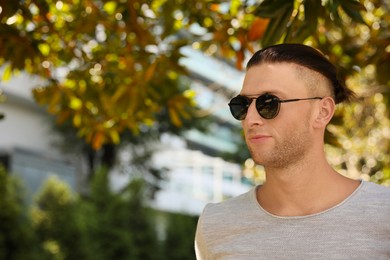 Photo of Handsome young man in stylish sunglasses at park, space for text