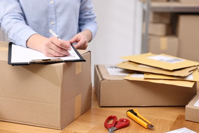 Parcel packing. Post office worker with clipboard writing notes at wooden table indoors, closeup