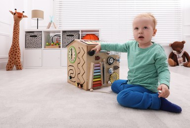 Cute little boy playing with busy board house on floor at home