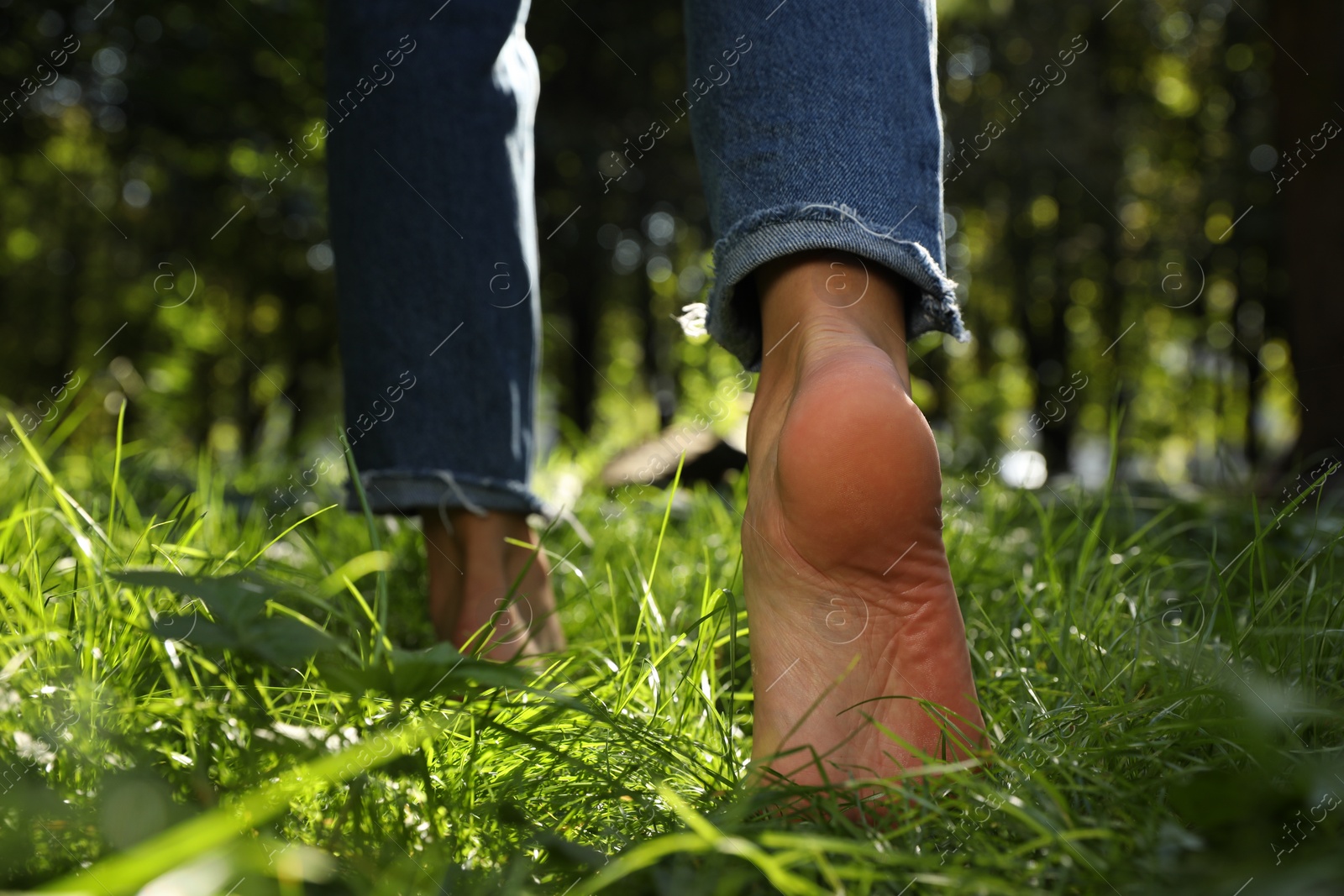 Photo of Woman walking barefoot on green grass in park, closeup