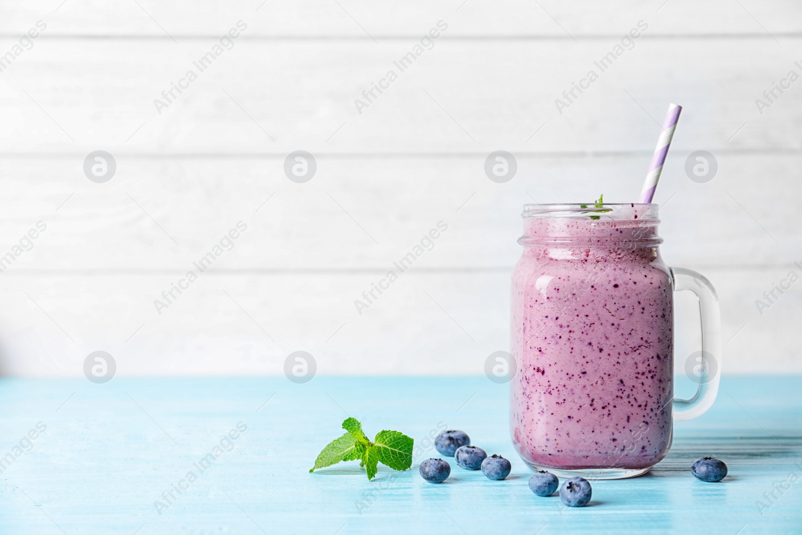 Photo of Tasty blueberry smoothie in mason jar on table against light background with space for text