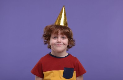 Photo of Cute little boy in party hat on purple background