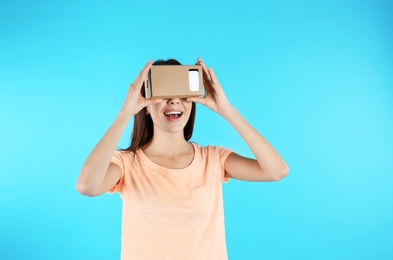 Photo of Young woman using cardboard virtual reality headset on color background