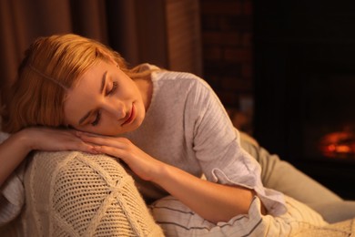 Photo of Beautiful young woman resting near fireplace at home