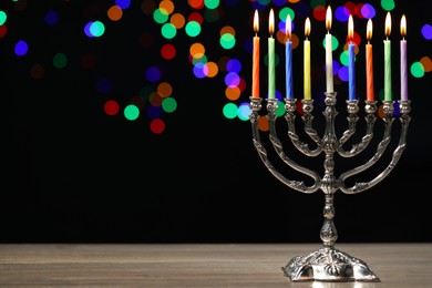 Hanukkah celebration. Menorah with burning candles on wooden table against dark background with blurred lights, space for text