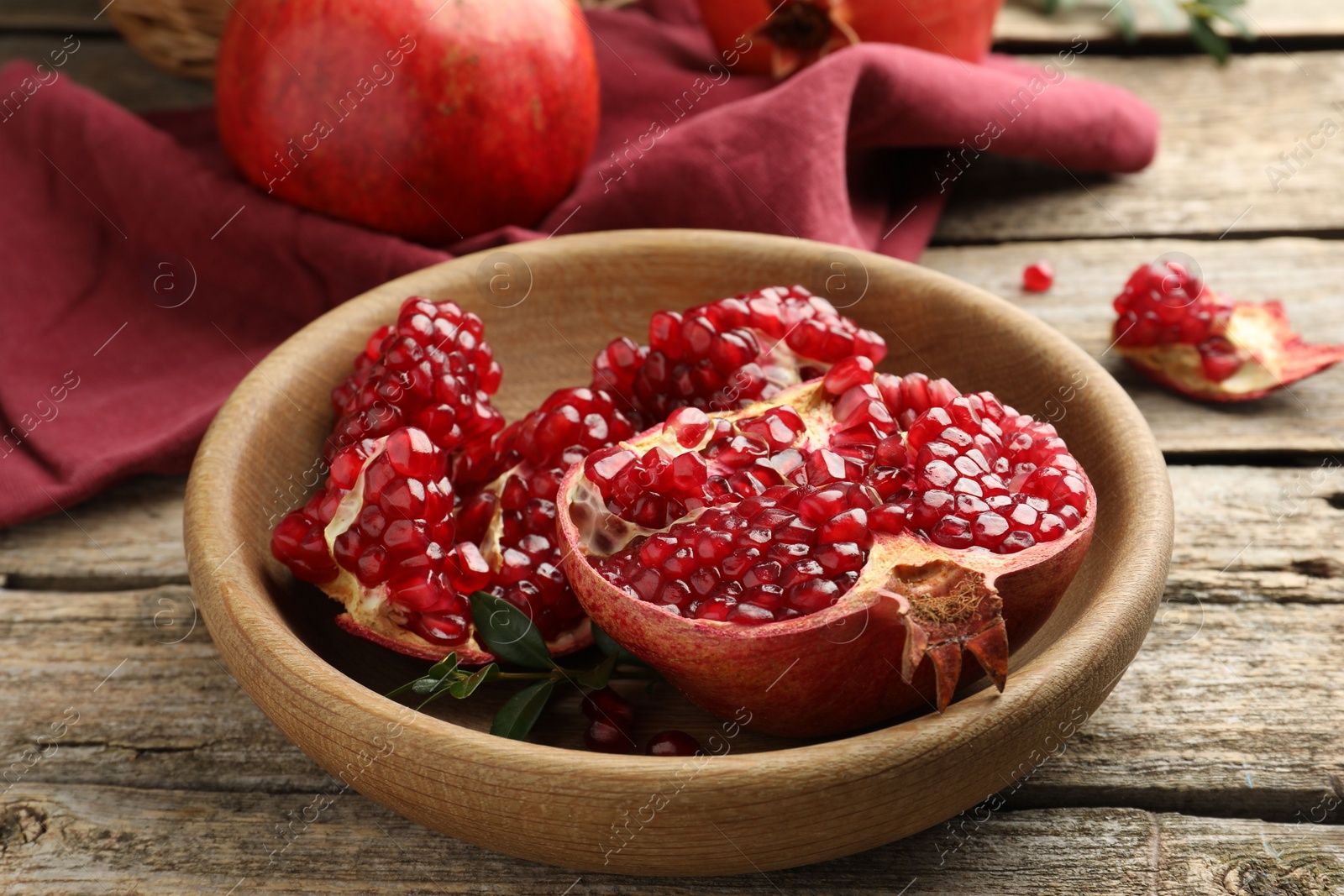 Photo of Fresh pomegranates and green leaves on wooden table, closeup