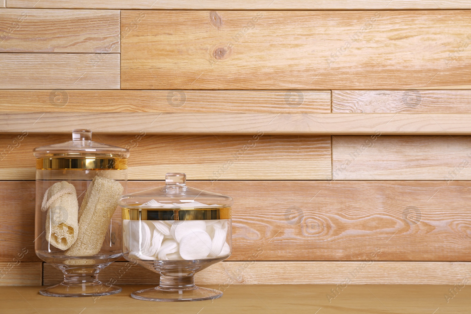 Photo of Composition of glass jar with cotton pads on table near wooden wall. Space for text