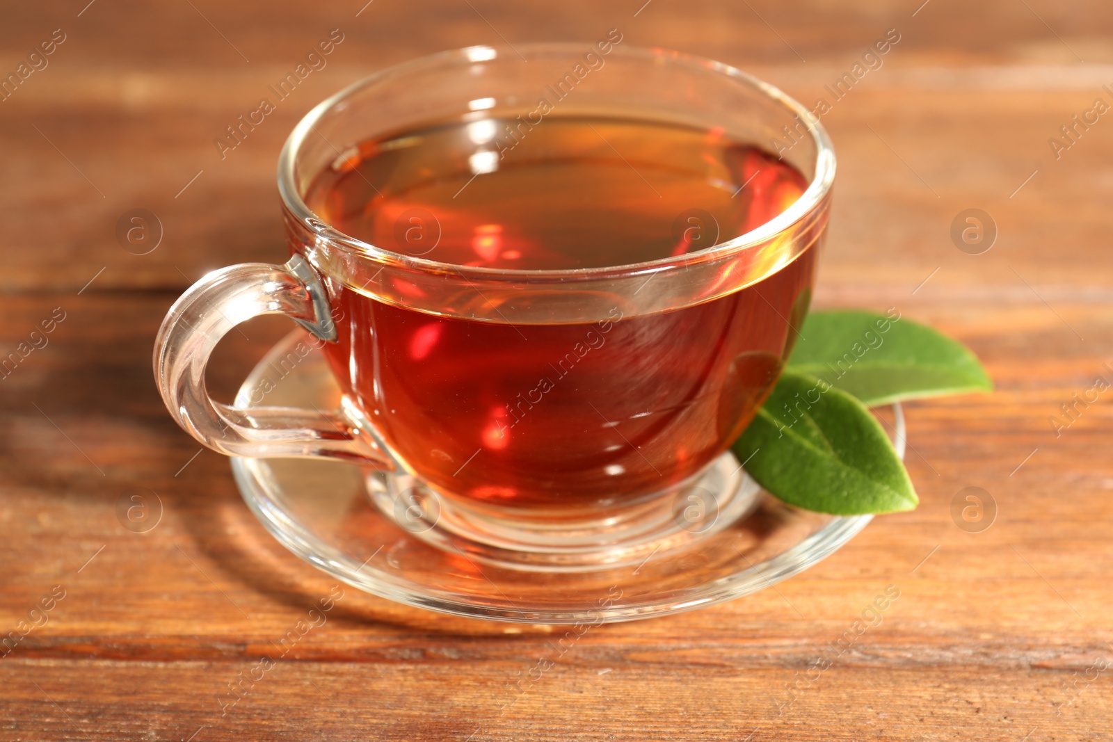 Photo of Aromatic tea in glass cup and green leaves on wooden table