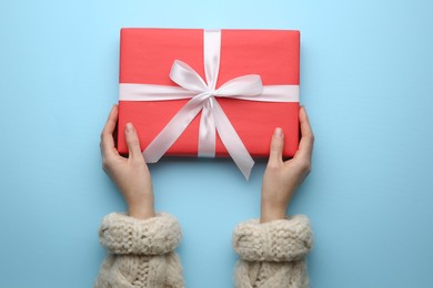 Woman holding red Christmas gift box on light blue background, top view