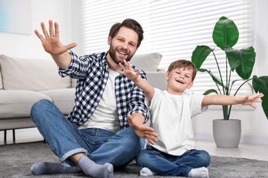 Photo of Happy dad and son having fun on carpet at home
