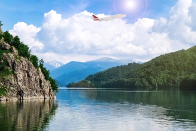 Image of Airplane flying over beautiful lake surrounded by mountains on sunny day