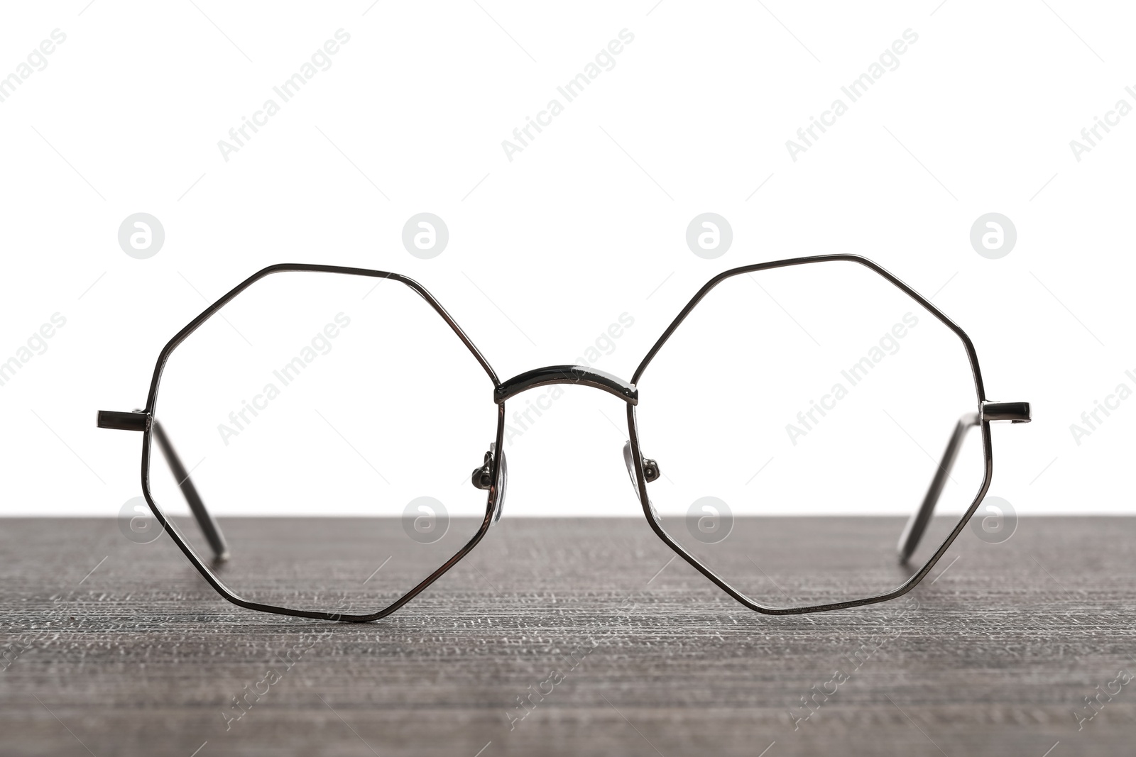 Photo of Stylish glasses with metal frame on wooden table against white background