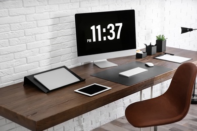 Modern workplace interior with computer and devices on table near brick wall