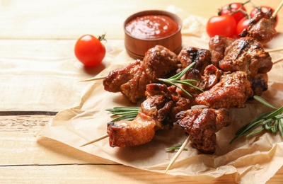 Photo of Delicious barbecued meat served with sauce and garnish on wooden background. Space for text