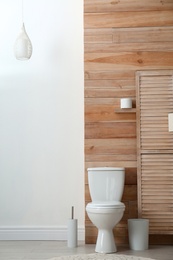Photo of Toilet bowl near wooden wall in modern bathroom interior