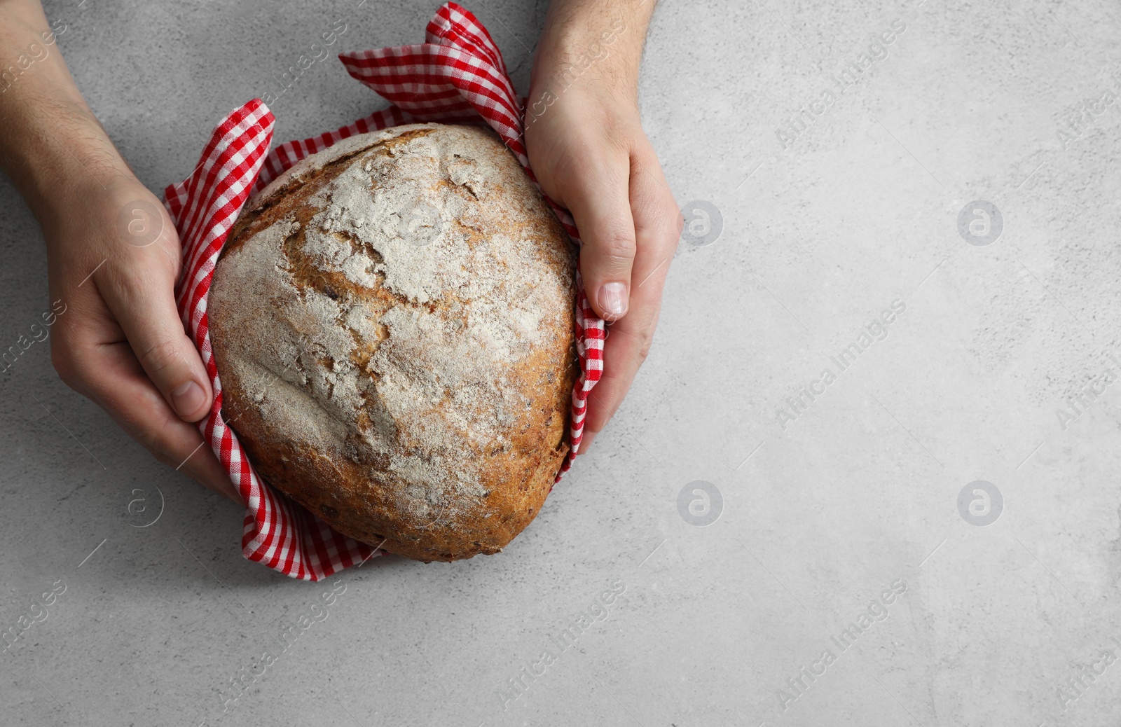 Photo of Man holding loaf of fresh bread at grey table, top view. Space for text