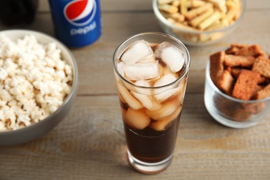 Photo of MYKOLAIV, UKRAINE - FEBRUARY 15, 2021: Glass of Pepsi and snacks on wooden table