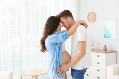 Young husband and his pregnant wife hugging at home