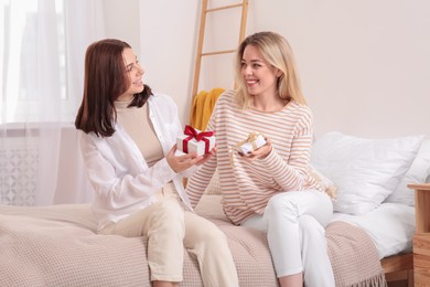 Smiling young women presenting gifts to each other on bed at home