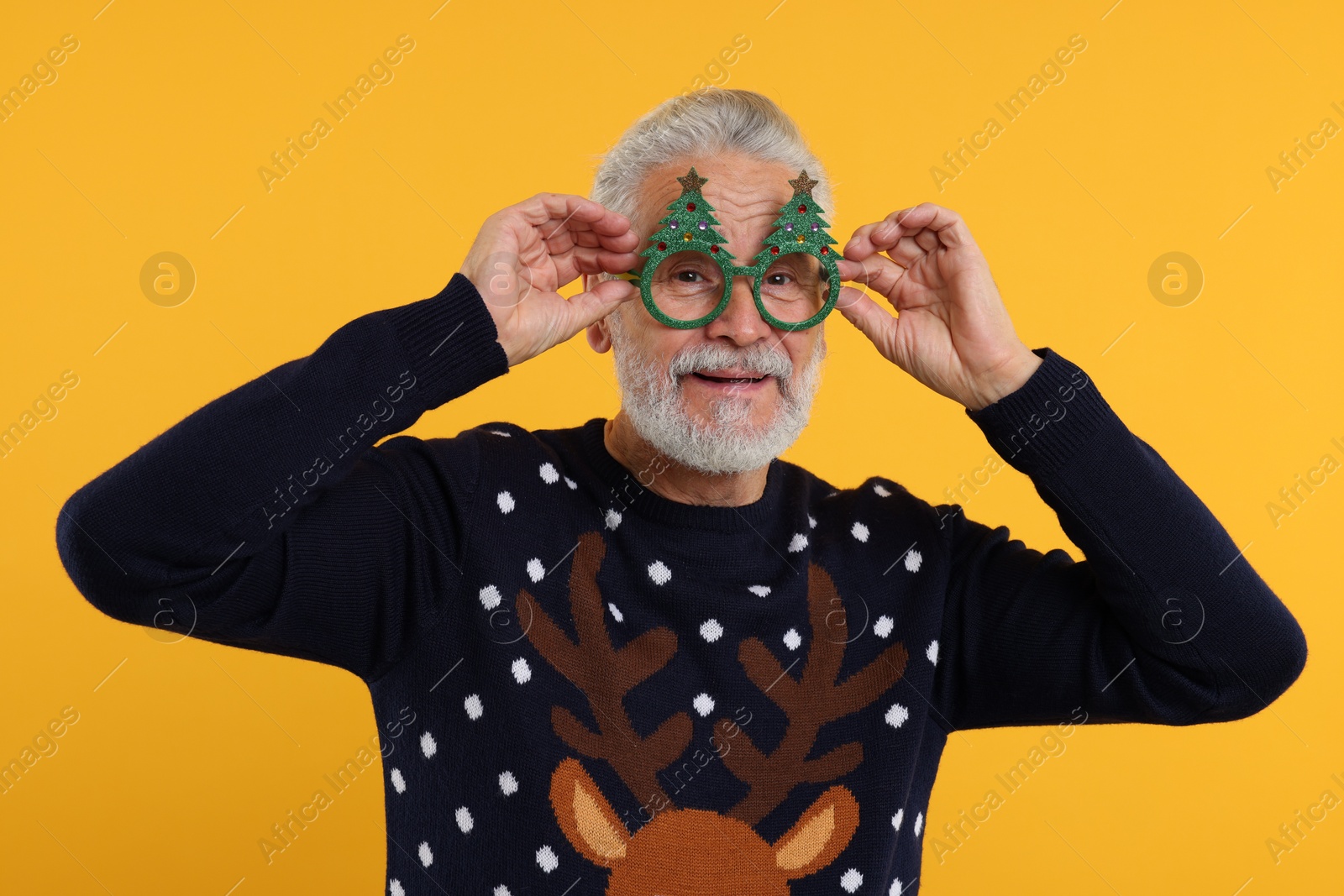 Photo of Senior man in Christmas sweater and funny glasses against orange background