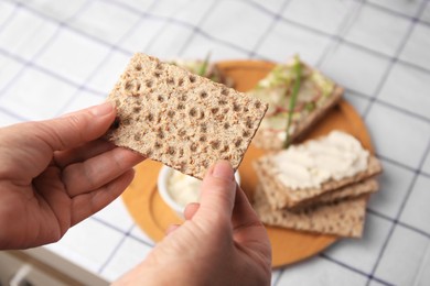 Photo of Woman holding fresh crunchy crispbread above table, closeup. Space for text