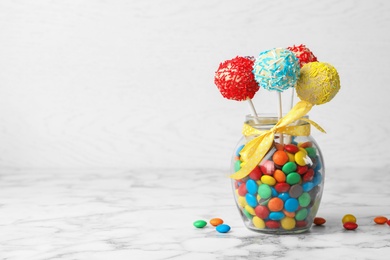 Photo of Yummy bright cake pops in glass jar full of candies on table. Space for text