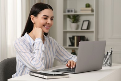 Happy woman working with laptop at white desk in room
