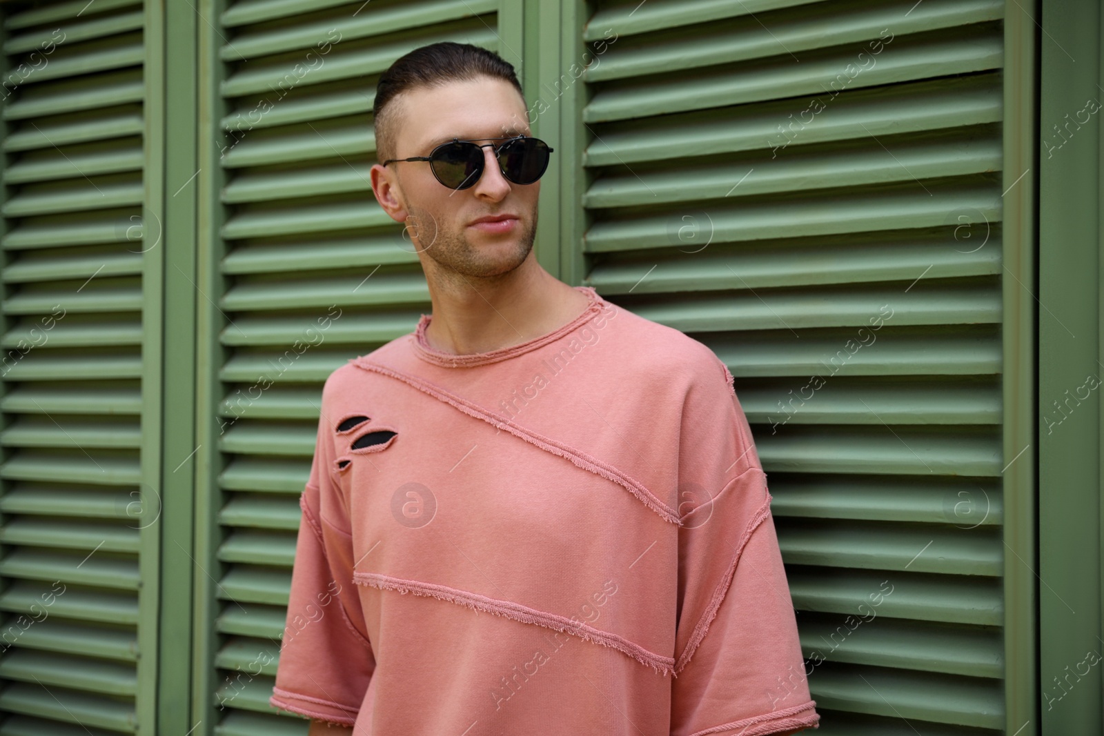 Photo of Handsome young man in stylish sunglasses near shutters