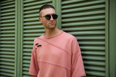 Photo of Handsome young man in stylish sunglasses near shutters