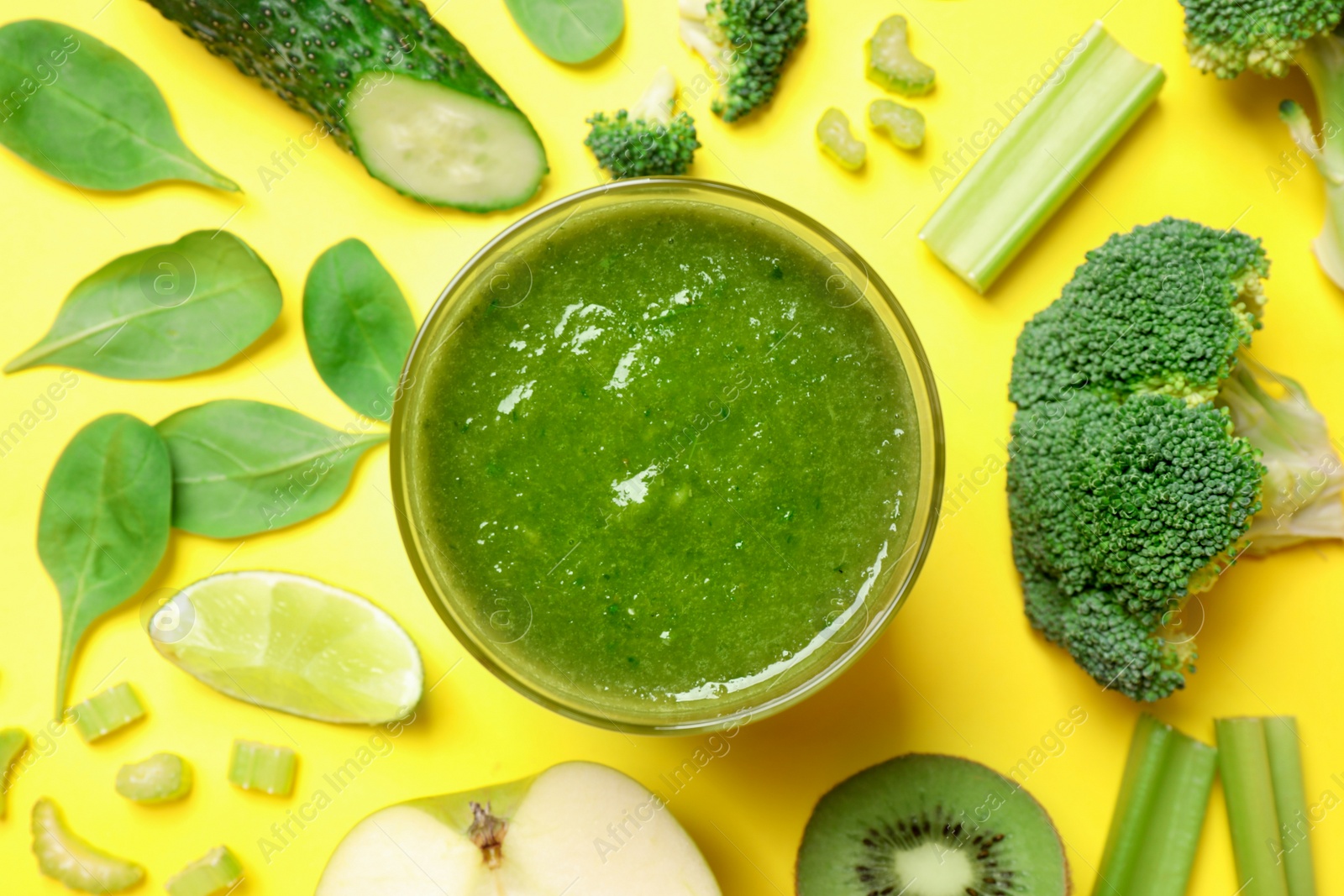 Photo of Delicious green juice and fresh ingredients on yellow background, flat lay