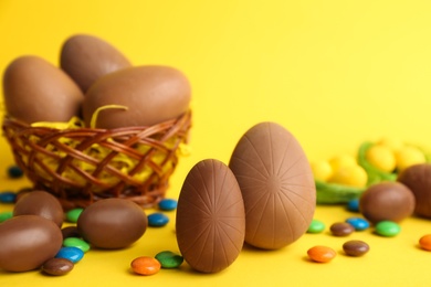 Sweet chocolate eggs and bright candies on yellow background