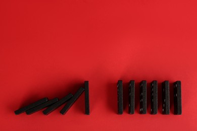 Photo of Black domino tiles on red background, flat lay. Space for text