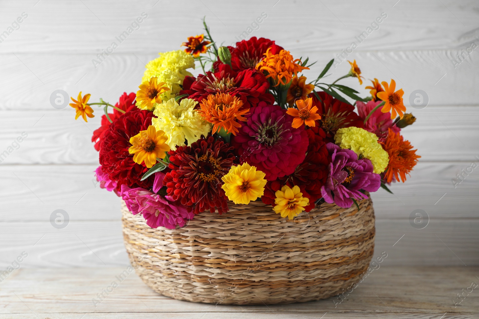Photo of Beautiful wild flowers in wicker basket on light wooden table