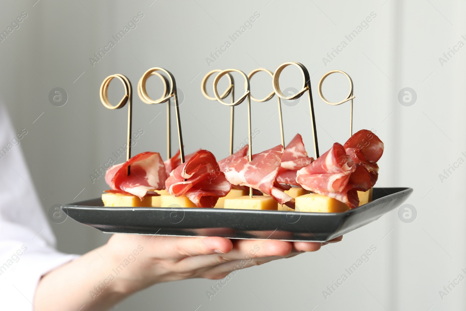 Photo of Woman holding plate of tasty canapes with ham and cheese indoors, closeup