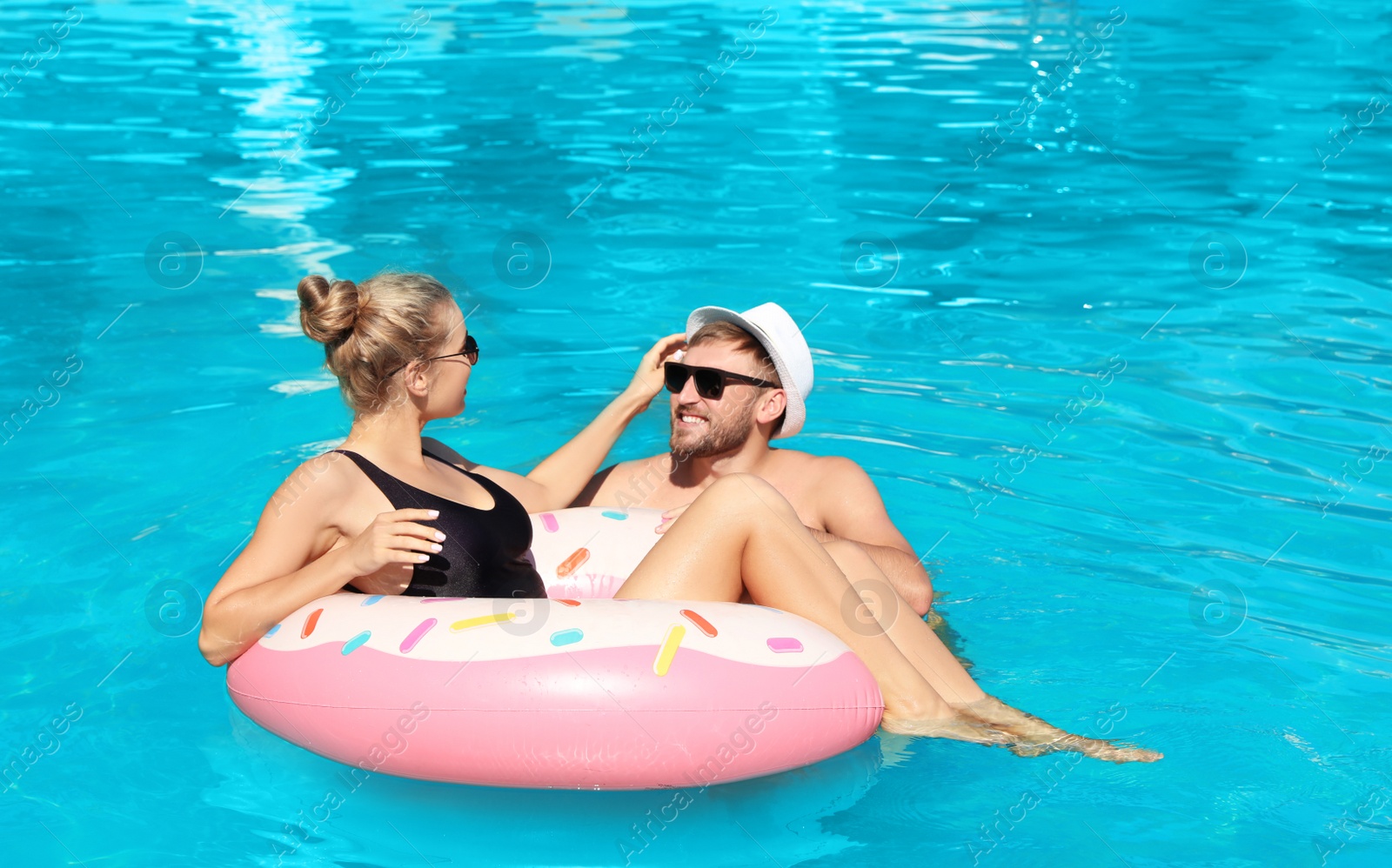 Photo of Happy young couple with inflatable ring in swimming pool