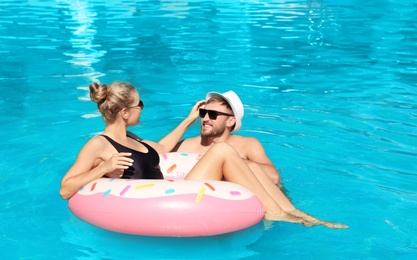 Happy young couple with inflatable ring in swimming pool