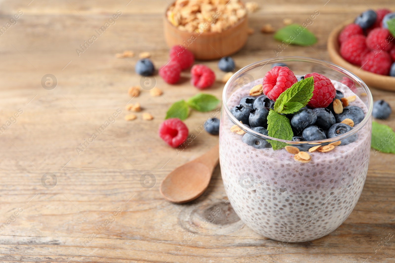 Photo of Delicious chia pudding with berries, granola and mint on wooden table, space for text