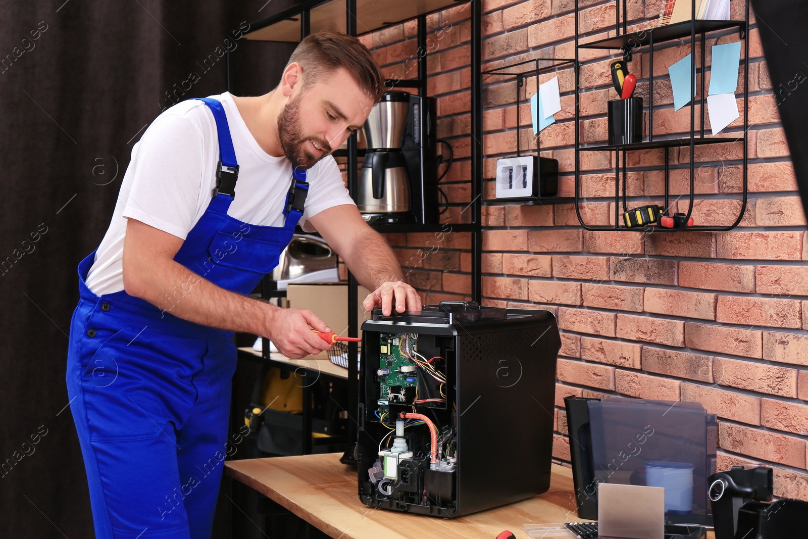 Photo of Repairman with screwdriver fixing coffee machine at table indoors