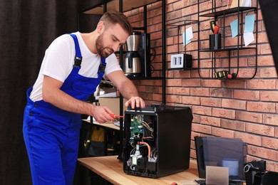 Photo of Repairman with screwdriver fixing coffee machine at table indoors