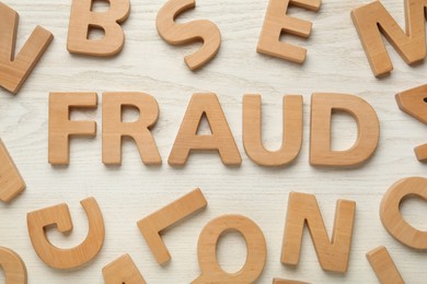 Photo of Word Fraud surrounded by wooden letters on white background, flat lay