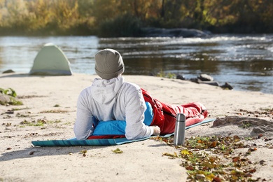 Male camper sitting in sleeping bag on wild beach. Space for text