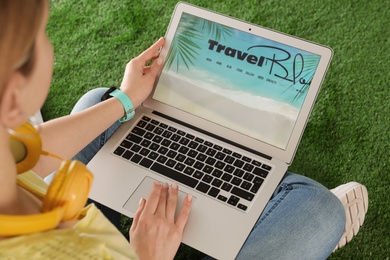 Photo of Woman holding laptop with open travel blogger site on artificial grass, closeup