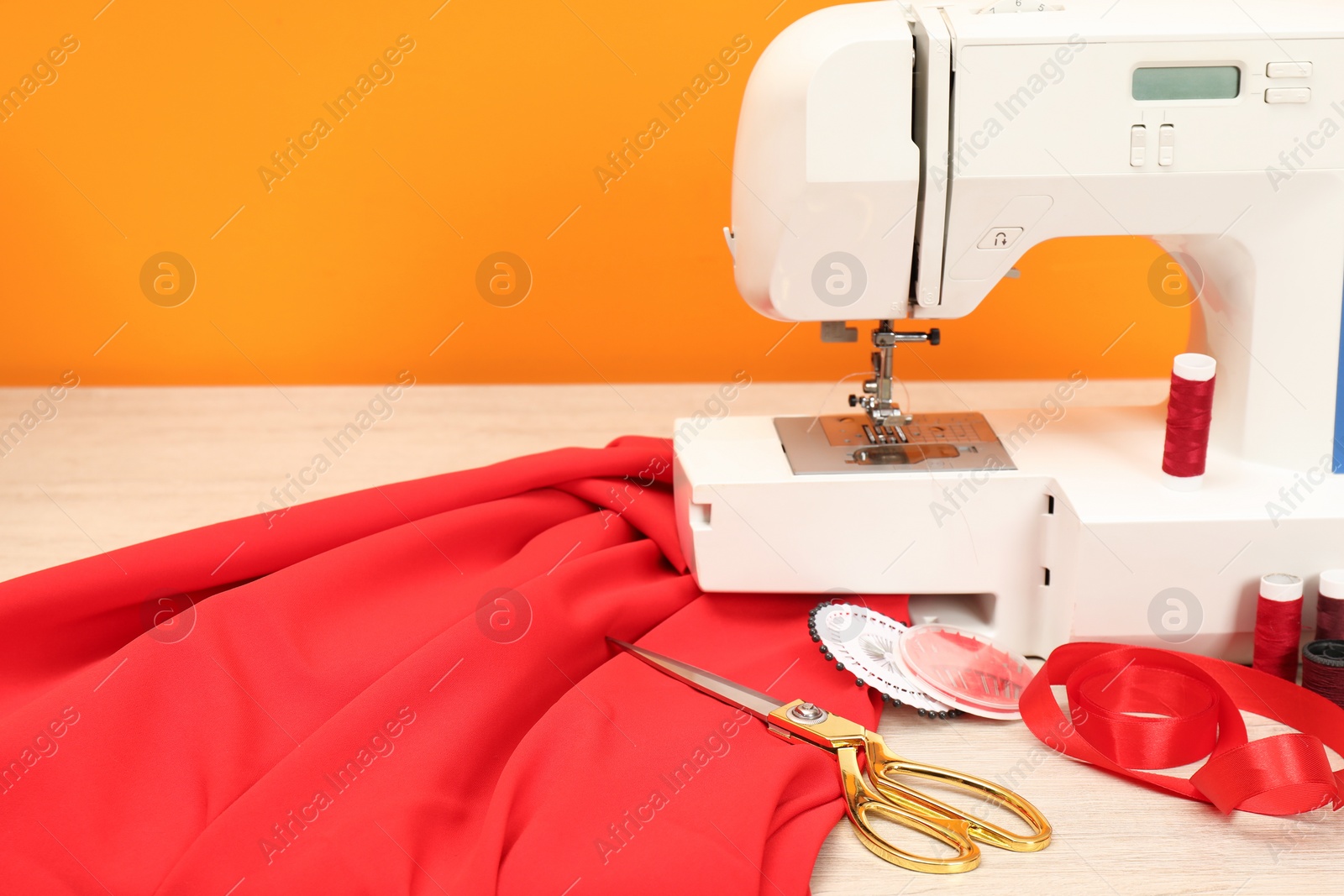 Photo of Modern sewing machine with cloth and craft accessories on wooden table near orange wall, closeup