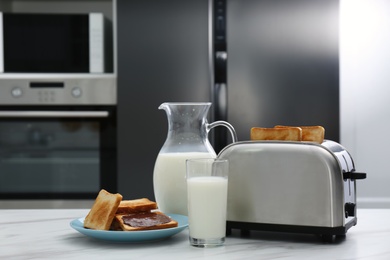 Modern toaster, bread slices with chocolate cream and milk on white marble table in kitchen