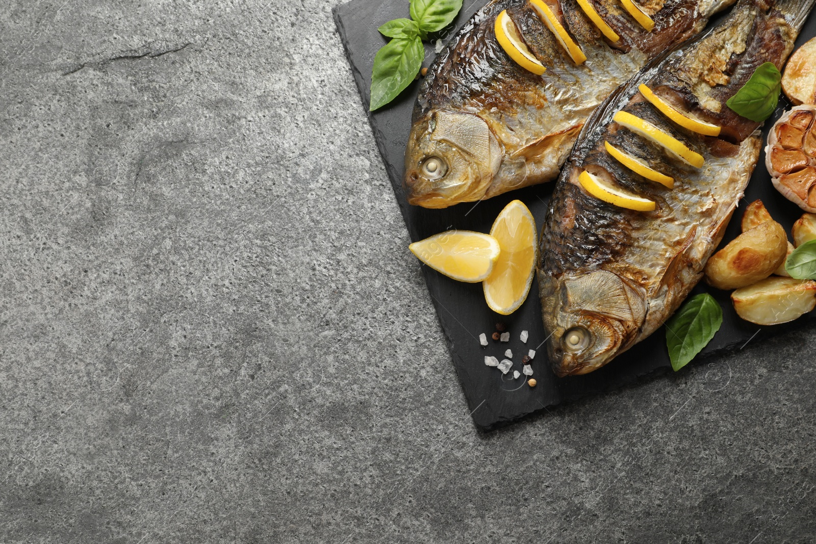 Photo of Tasty homemade roasted crucian carps served on grey table, top view and space for text. River fish